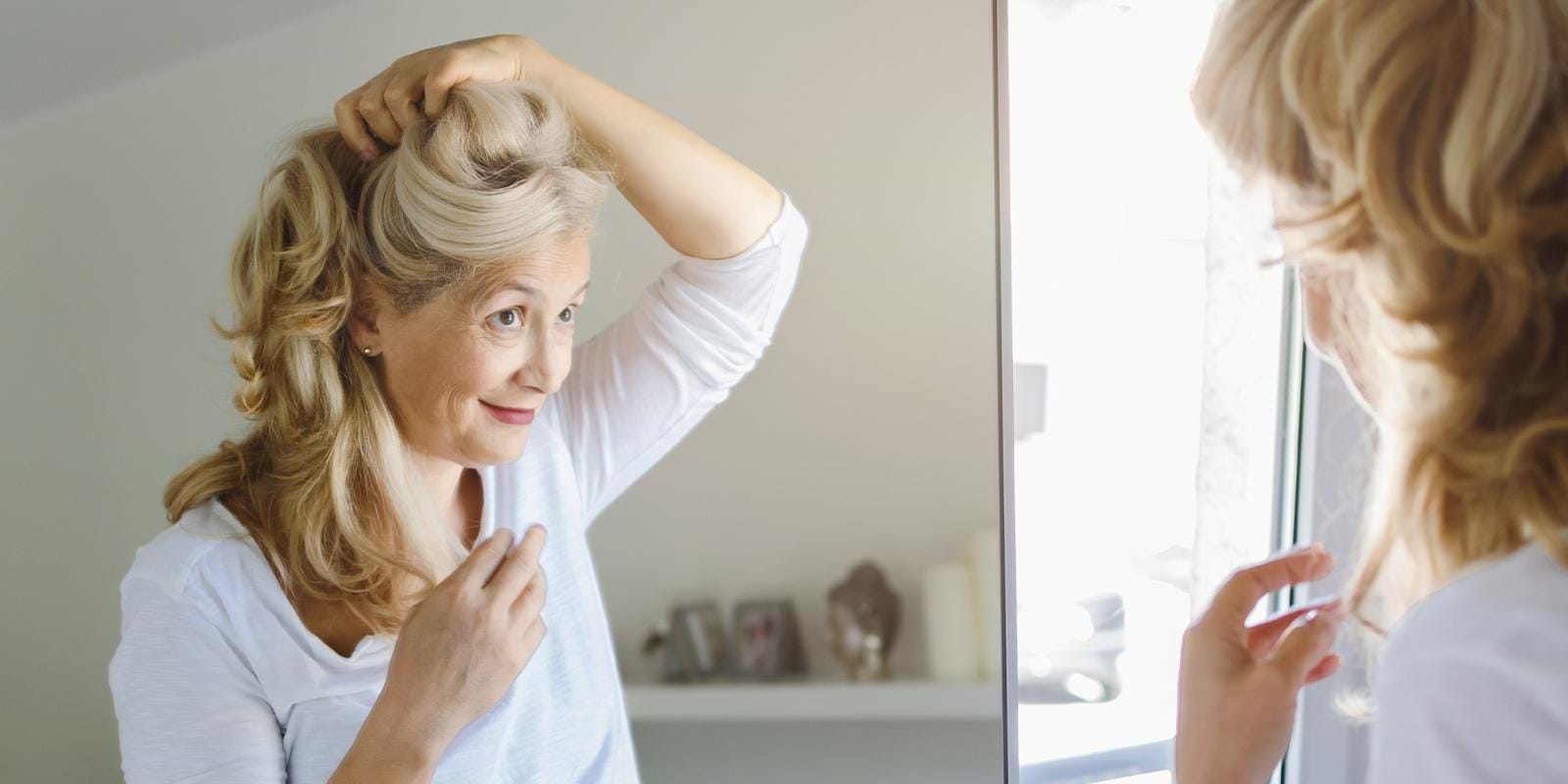 Blonde woman looking at hair in the mirror and smiling