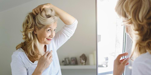 Blonde woman looking at hair in the mirror and smiling