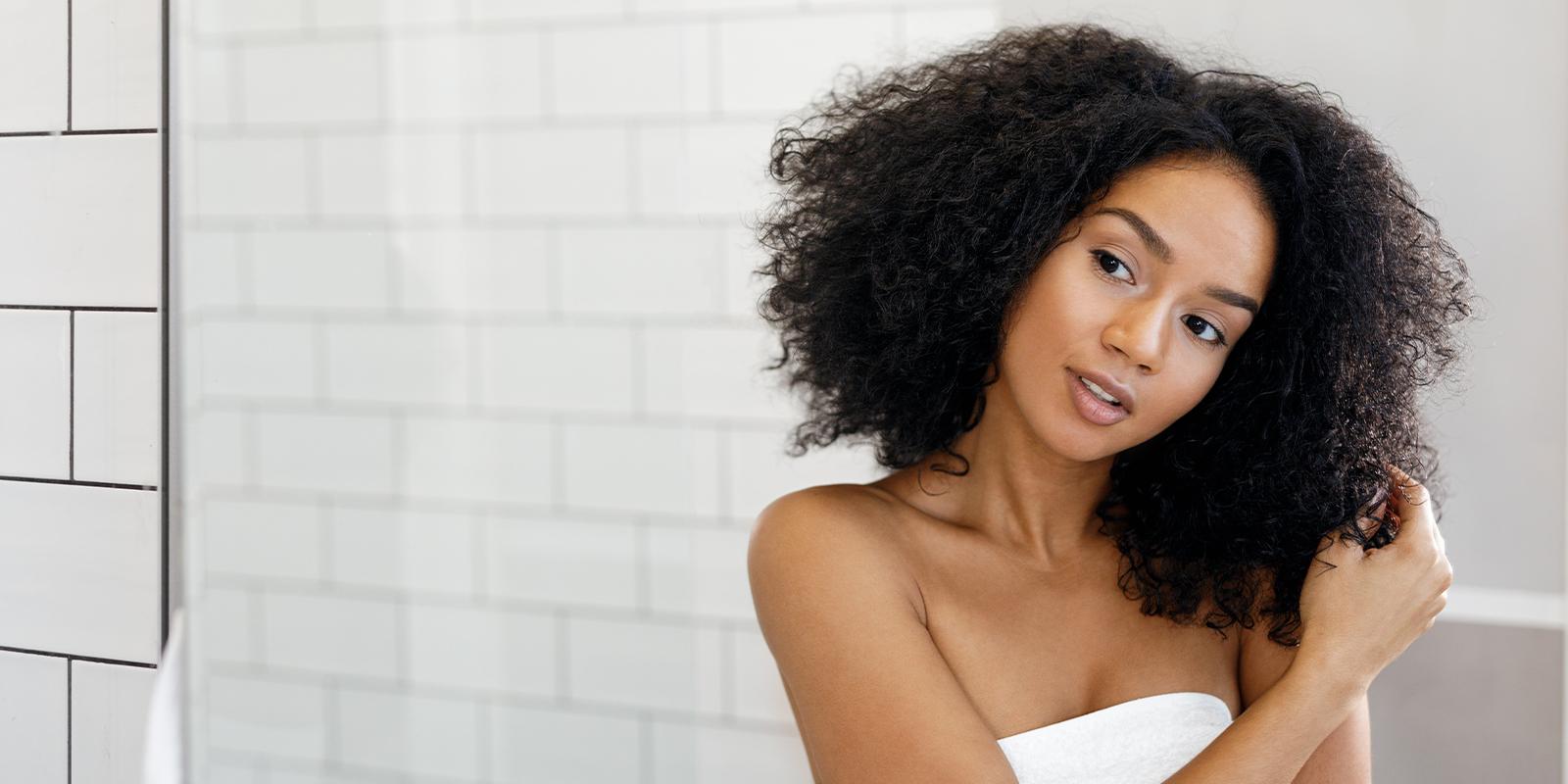 Black woman thinking and looking at dark curly hair in the mirror