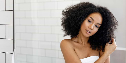 Black woman thinking and looking at dark curly hair in the mirror
