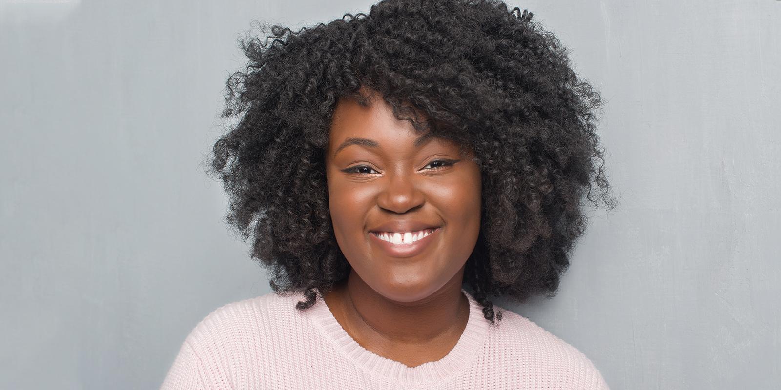 smiling woman with short curly black hair wearing a pink top