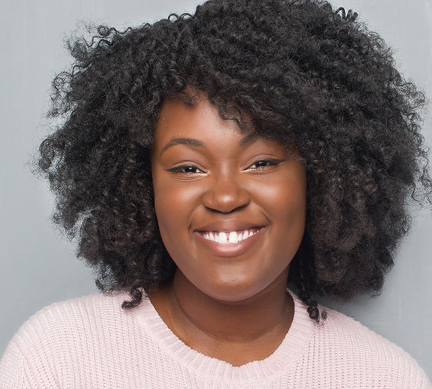 smiling woman with short curly black hair wearing a pink top