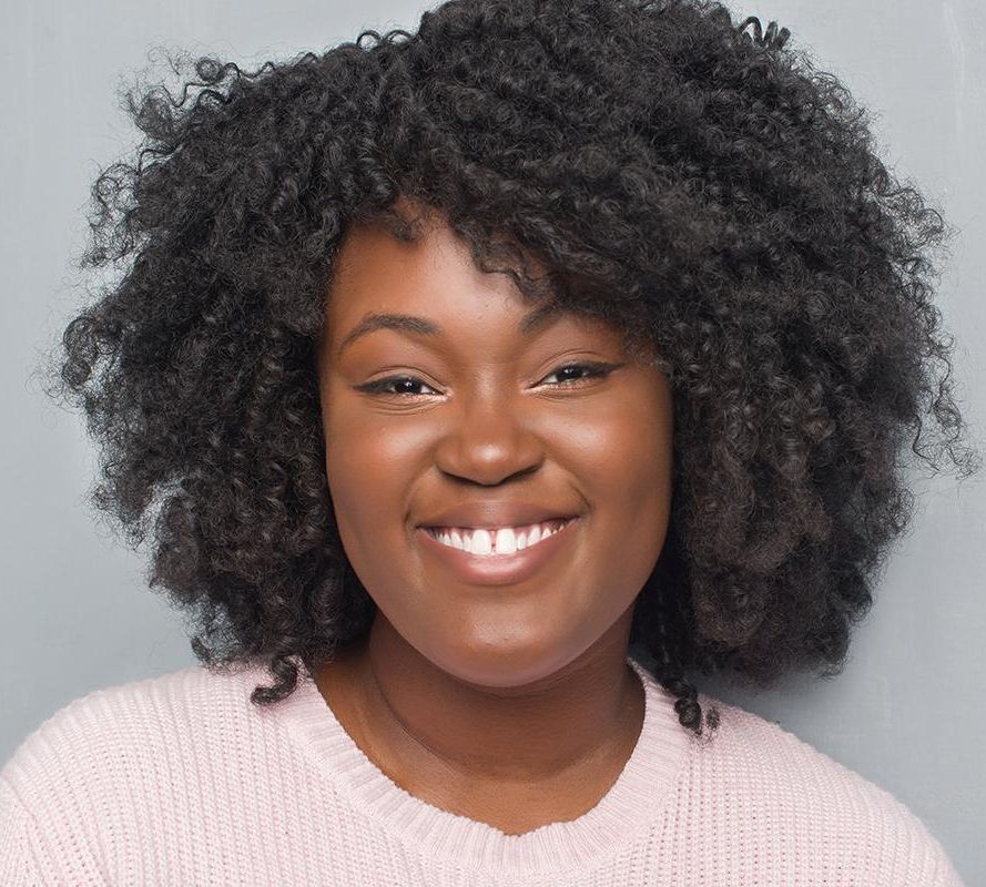 smiling woman with short curly black hair wearing a pink top
