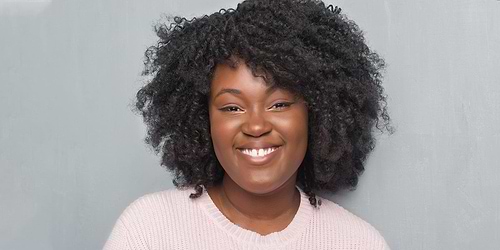 smiling woman with short curly black hair wearing a pink top