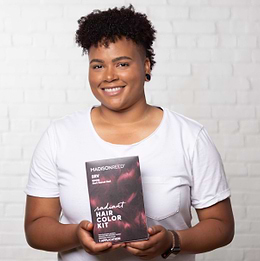 Woman with short coily hair smiling and holding Madison Reed Radiant Hair Color Kit